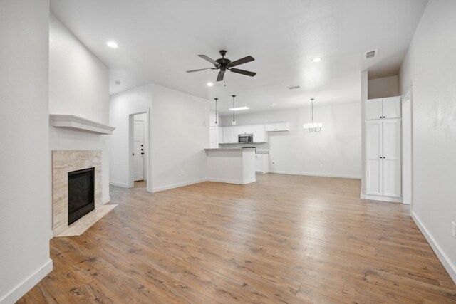 unfurnished living room featuring ceiling fan with notable chandelier and light hardwood / wood-style floors