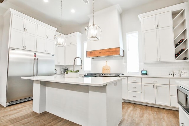 kitchen with built in appliances, light countertops, white cabinetry, and light wood-style floors