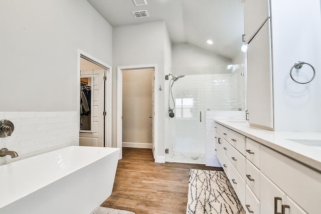 full bath with visible vents, wood finished floors, a walk in closet, a freestanding tub, and a shower stall