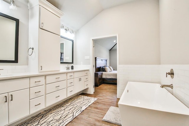 full bathroom with lofted ceiling, a freestanding tub, wood finished floors, wainscoting, and double vanity