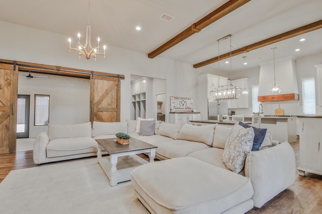 living room with a barn door, beam ceiling, wood finished floors, and visible vents