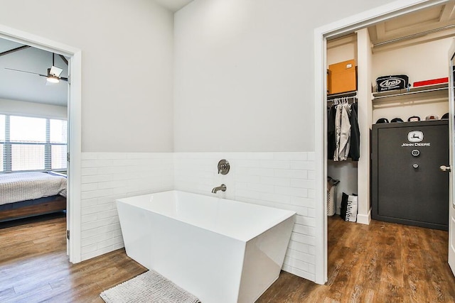 full bath featuring a freestanding tub, wood finished floors, tile walls, a spacious closet, and wainscoting