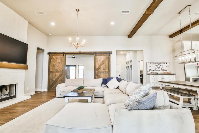 living area with an inviting chandelier, a barn door, visible vents, and wood finished floors