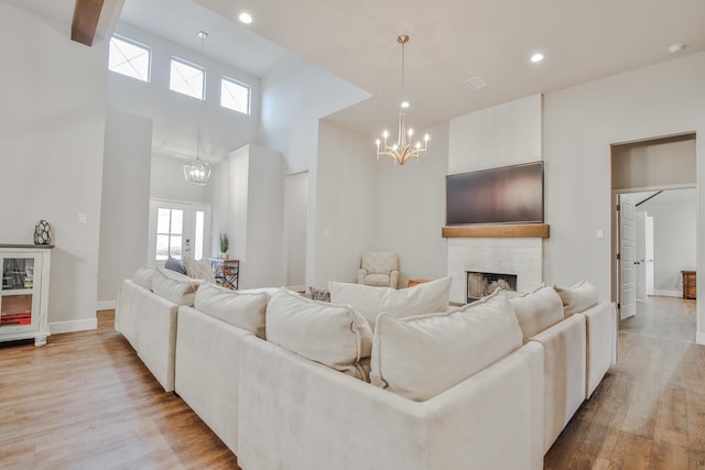 living room with a notable chandelier, recessed lighting, a large fireplace, light wood-type flooring, and baseboards