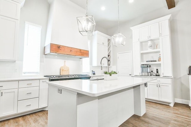 kitchen featuring light wood finished floors, white cabinets, an island with sink, light countertops, and open shelves