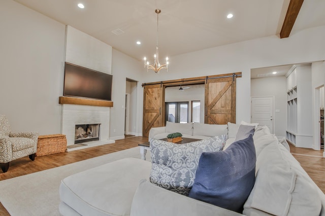 living room with a fireplace with raised hearth, a barn door, recessed lighting, light wood-style floors, and beamed ceiling