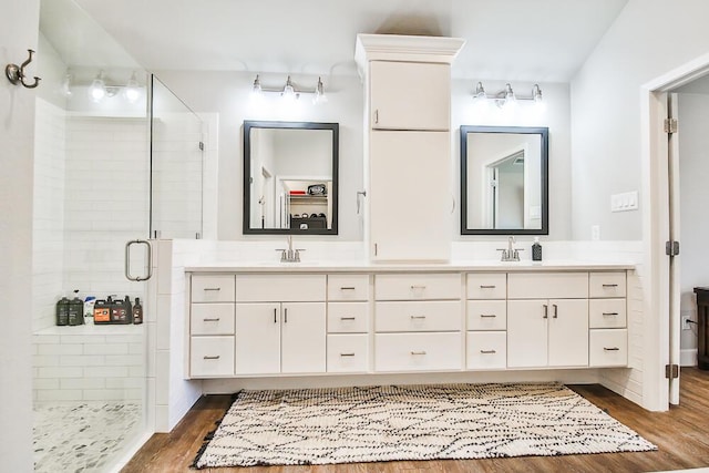 bathroom with a sink, a shower stall, double vanity, and wood finished floors