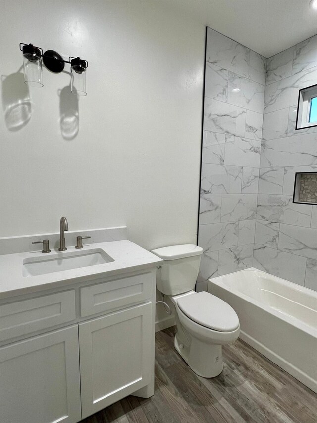 full bathroom with tiled shower / bath combo, vanity, hardwood / wood-style floors, and toilet