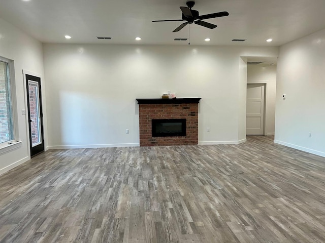 unfurnished living room with hardwood / wood-style flooring, ceiling fan, and a brick fireplace