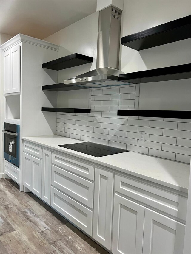 kitchen featuring white cabinets, wall chimney exhaust hood, and black appliances