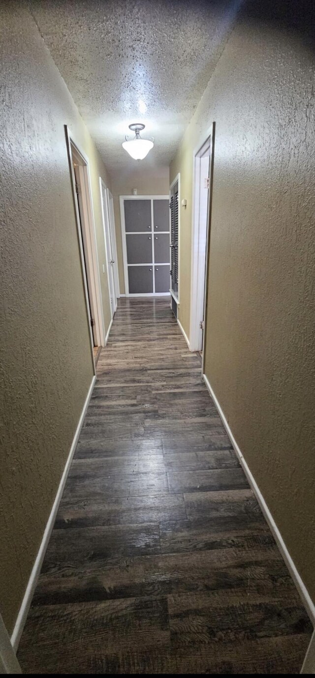 corridor with dark wood finished floors, baseboards, and a textured wall