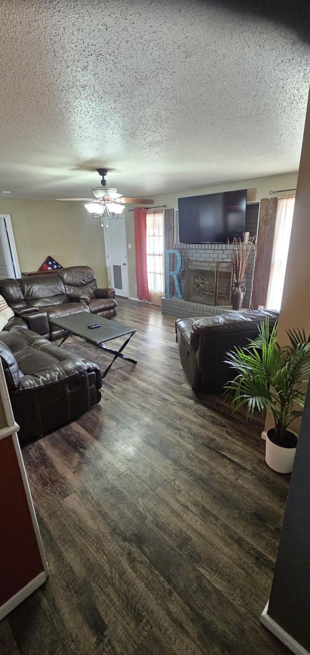 living area featuring a textured ceiling, wood finished floors, a ceiling fan, and a brick fireplace