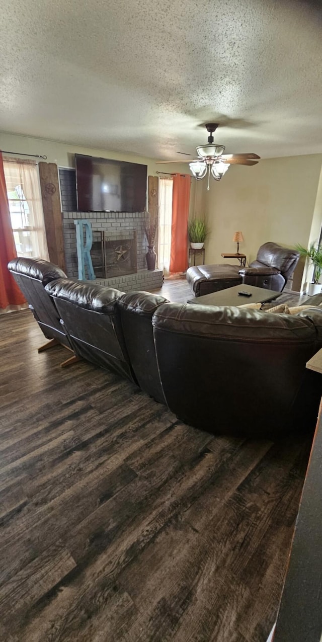 living room with ceiling fan, a textured ceiling, dark wood-style flooring, and a fireplace