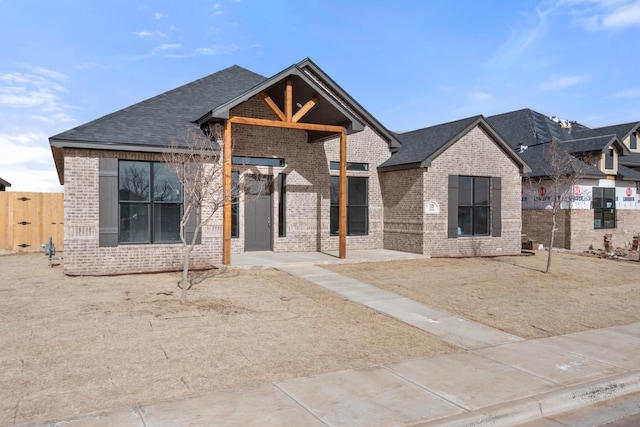 view of front of house with fence, brick siding, and roof with shingles