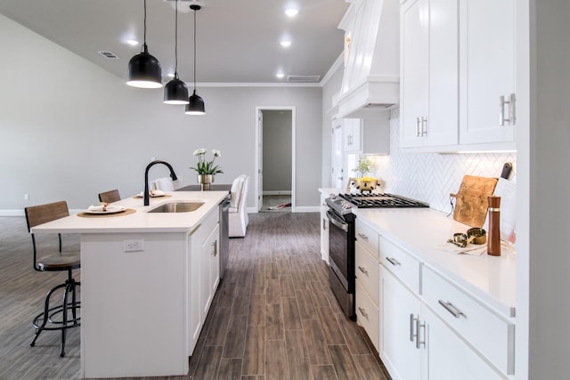 kitchen featuring an island with sink, sink, white cabinets, custom exhaust hood, and gas range