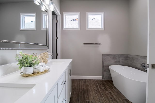 full bath featuring baseboards, wood finish floors, double vanity, a freestanding tub, and a sink