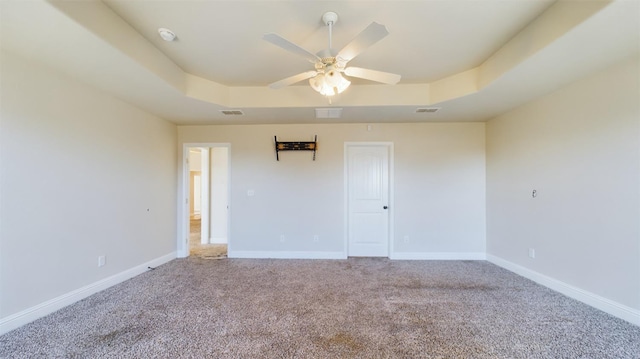 empty room featuring a tray ceiling, carpet floors, and ceiling fan