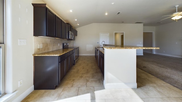 kitchen with sink, decorative backsplash, electric range, light stone counters, and a center island with sink