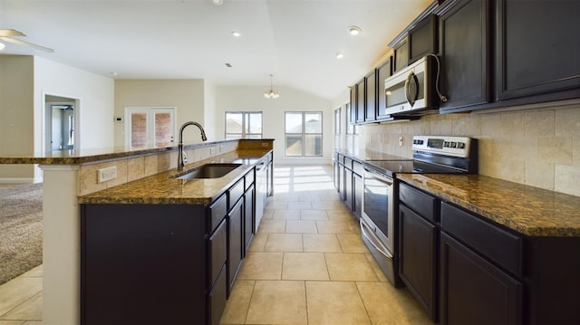 kitchen featuring sink, dark stone countertops, backsplash, stainless steel appliances, and an island with sink