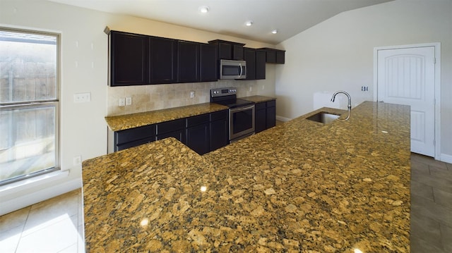 kitchen with vaulted ceiling, stainless steel appliances, sink, and an island with sink