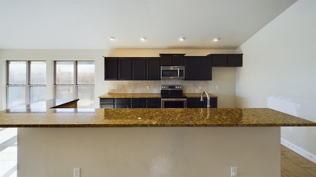 kitchen featuring stainless steel appliances, sink, dark stone countertops, and a large island with sink