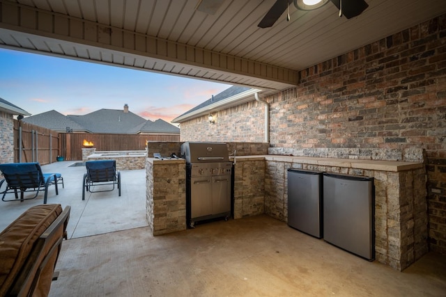 patio terrace at dusk featuring a grill, ceiling fan, and exterior kitchen