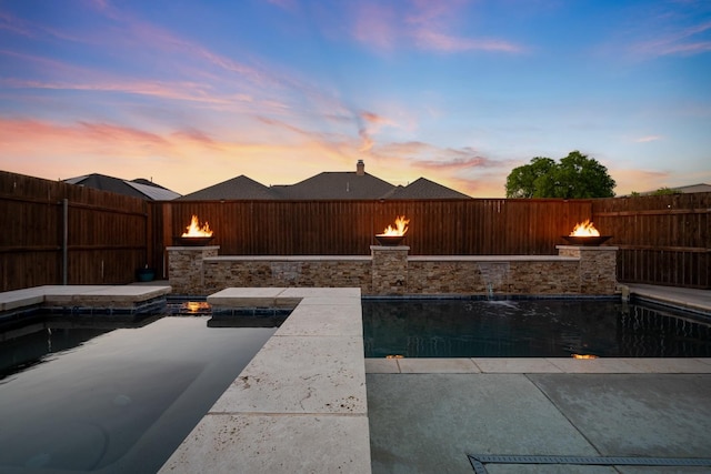 pool at dusk featuring pool water feature and a fire pit