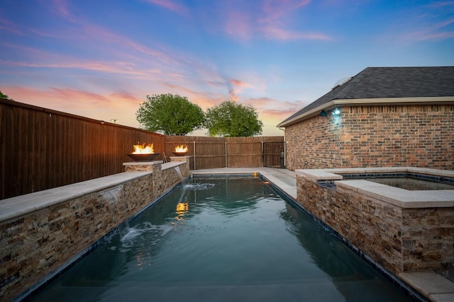 pool at dusk featuring pool water feature and an in ground hot tub