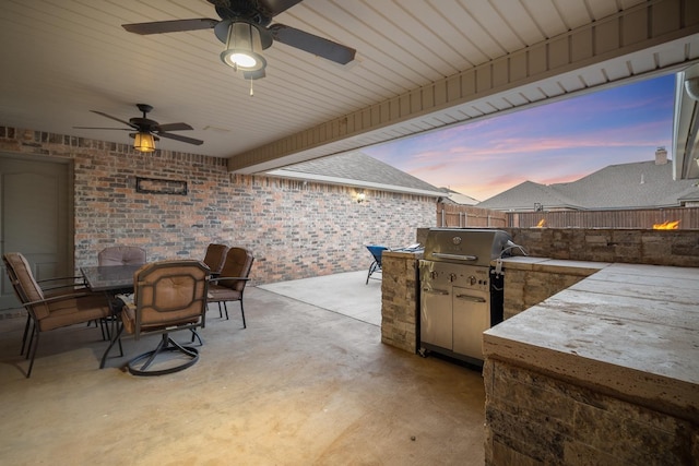 patio terrace at dusk with ceiling fan and exterior kitchen