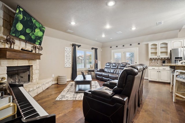 living room with dark hardwood / wood-style flooring, a stone fireplace, and a textured ceiling