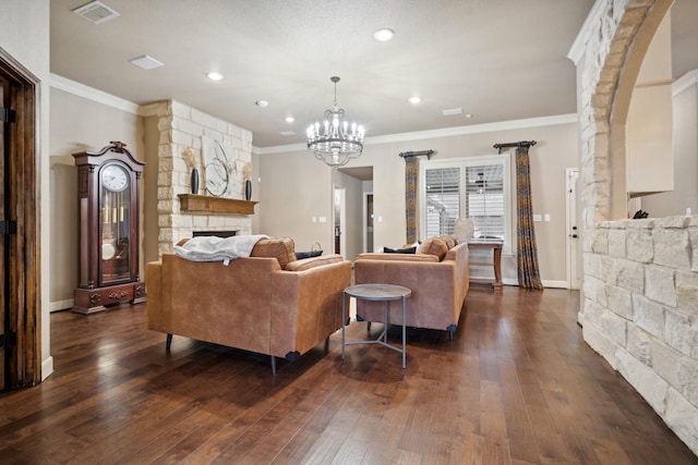 living room featuring ornamental molding, a stone fireplace, dark wood-type flooring, and an inviting chandelier