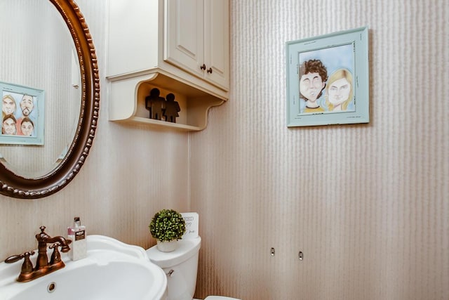 half bathroom with toilet, wallpapered walls, and a sink