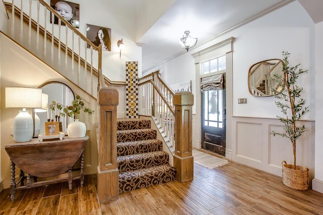 foyer with stairway, a decorative wall, a towering ceiling, wainscoting, and wood finished floors