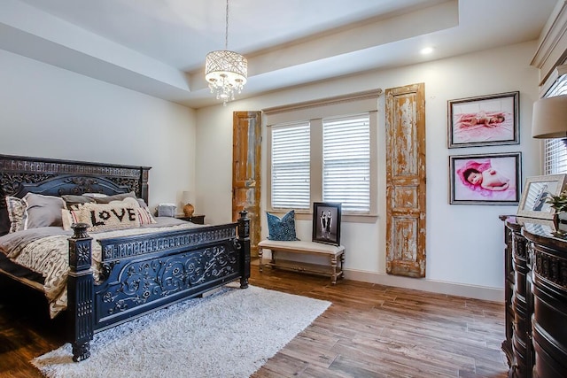 bedroom featuring recessed lighting, wood finished floors, baseboards, a raised ceiling, and a notable chandelier