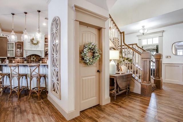 foyer entrance with crown molding, a wainscoted wall, stairs, visible vents, and wood finished floors