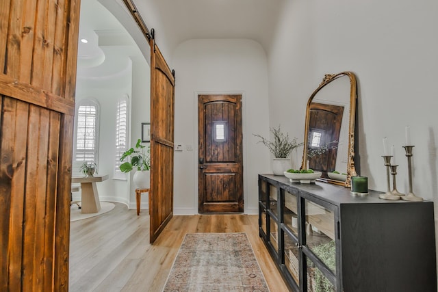 entrance foyer with light wood finished floors, a barn door, a high ceiling, and baseboards