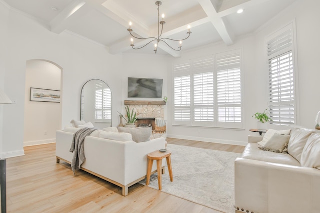 living area featuring arched walkways, a fireplace, light wood-style flooring, a chandelier, and baseboards