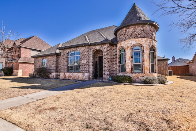 view of front of home featuring stone siding, brick siding, fence, and roof with shingles