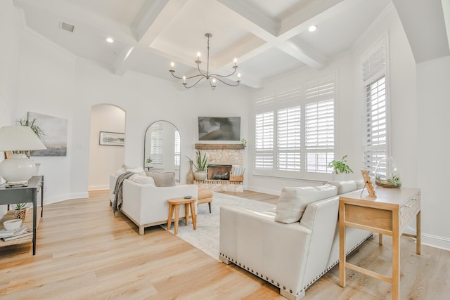 living room with light wood finished floors, visible vents, arched walkways, baseboards, and a stone fireplace