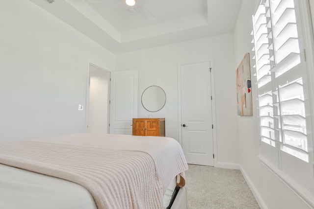 bedroom with light carpet, baseboards, and a raised ceiling