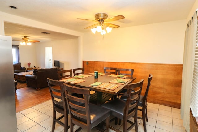 tiled dining space featuring wooden walls and ceiling fan