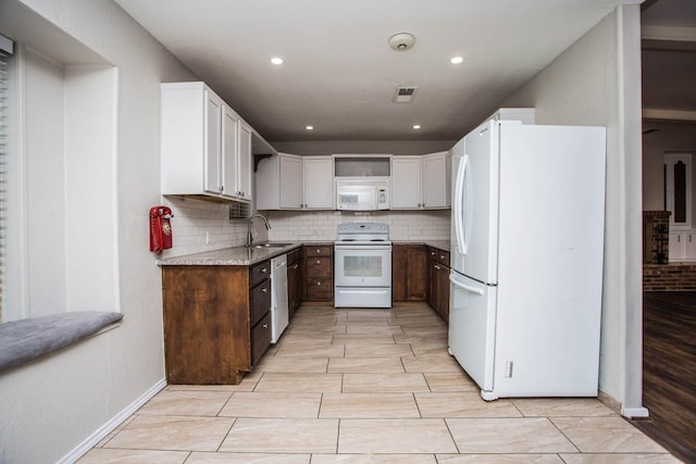 kitchen with backsplash, a sink, light stone counters, and white appliances