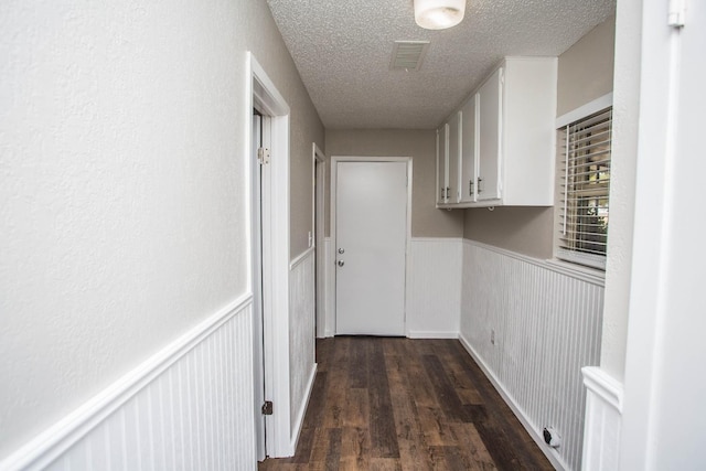corridor featuring a wainscoted wall, visible vents, dark wood-style floors, and a textured ceiling