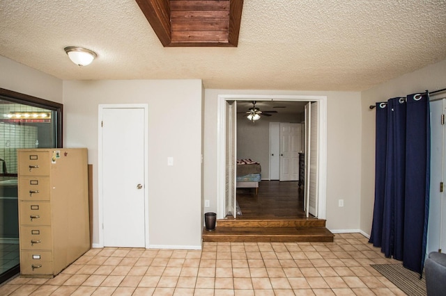 interior space with light tile patterned floors, baseboards, ceiling fan, and a textured ceiling