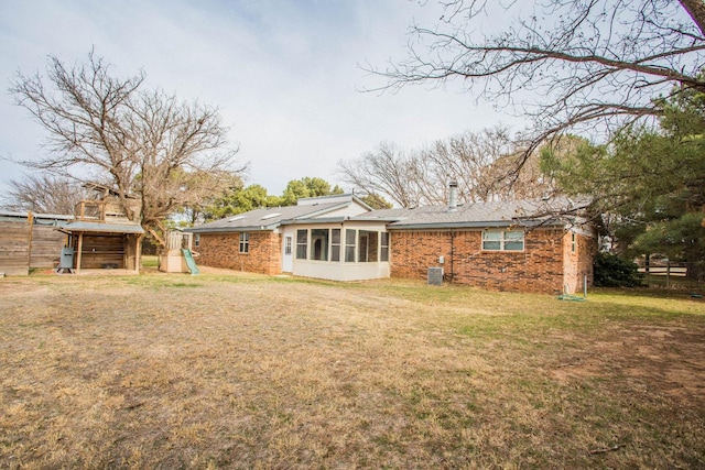 rear view of house with a lawn, a sunroom, central AC, and brick siding