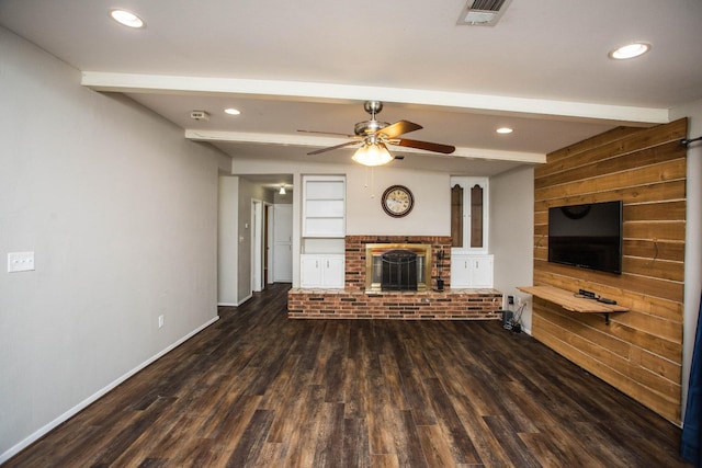 unfurnished living room featuring a brick fireplace, beam ceiling, visible vents, a ceiling fan, and wood finished floors