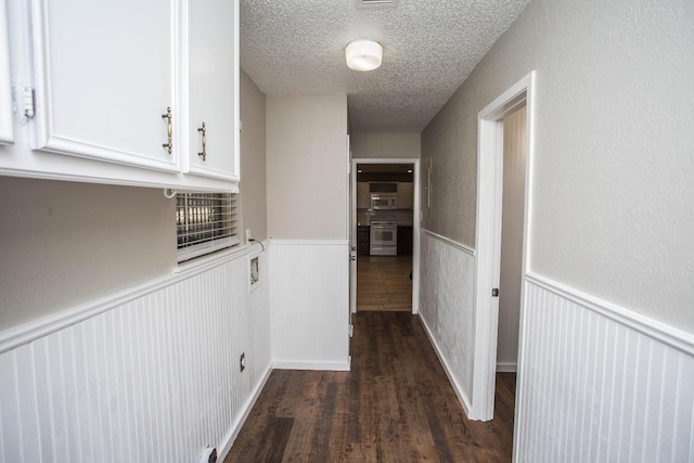 hallway featuring a wainscoted wall, dark wood finished floors, and a textured ceiling