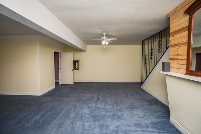 unfurnished room with dark colored carpet, stairway, baseboards, a textured ceiling, and ceiling fan