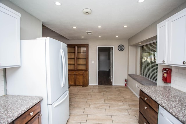 kitchen with backsplash, freestanding refrigerator, light stone countertops, white cabinets, and recessed lighting