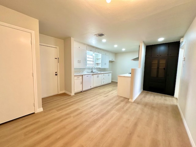 kitchen with light wood finished floors, white dishwasher, white cabinetry, and light countertops